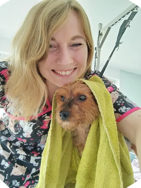 Camille, la toiletteuse, sèche un petit chien dans une serviette verte